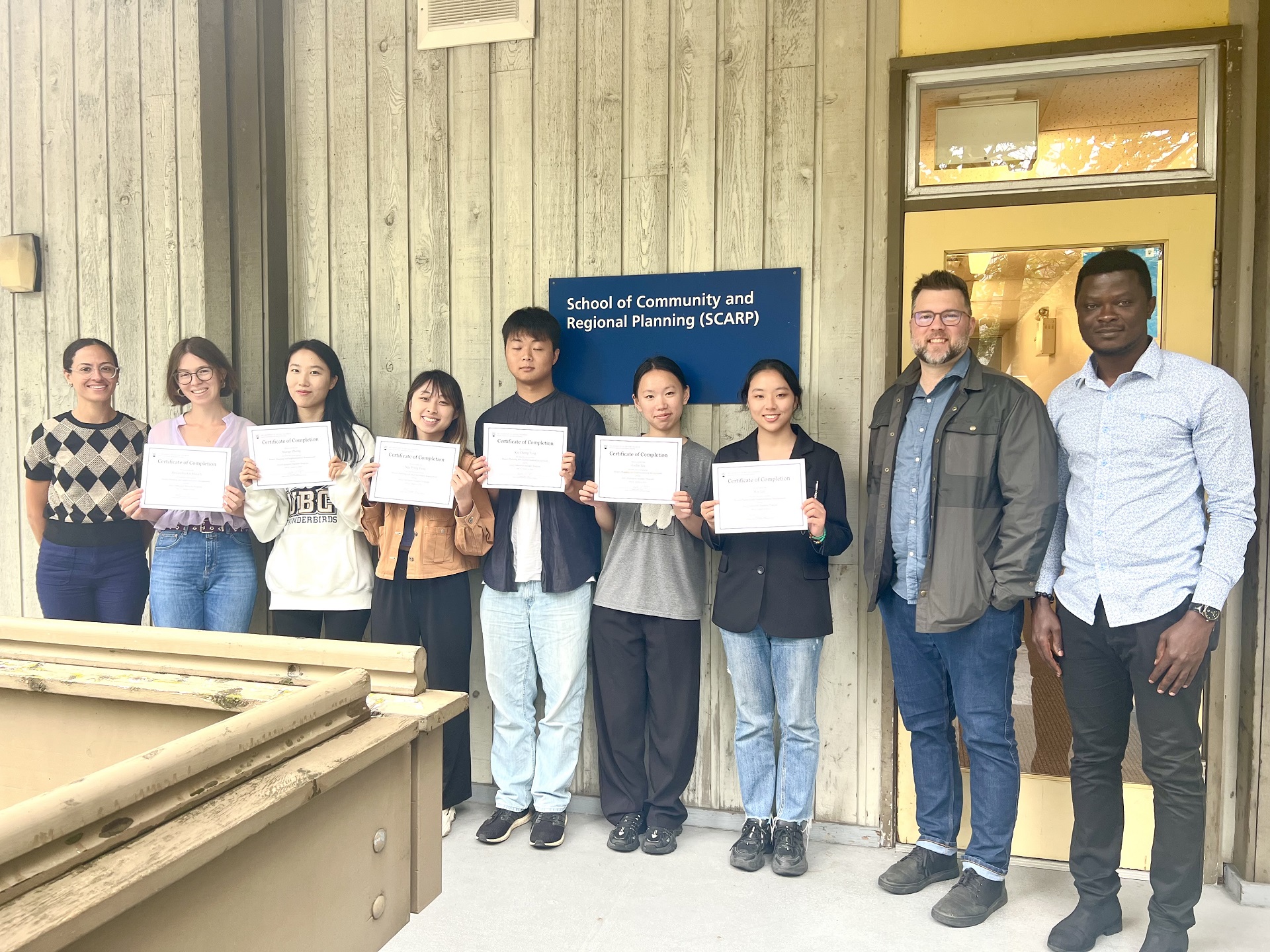 Students holding certificates of completion, flanked by their instructors
