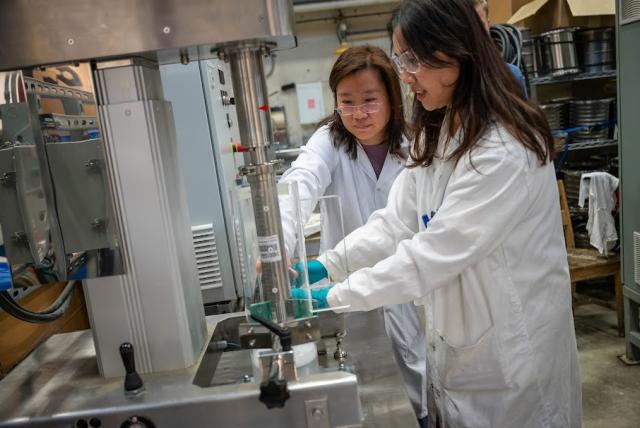 Two people in lab equipment utilize a lab machine.