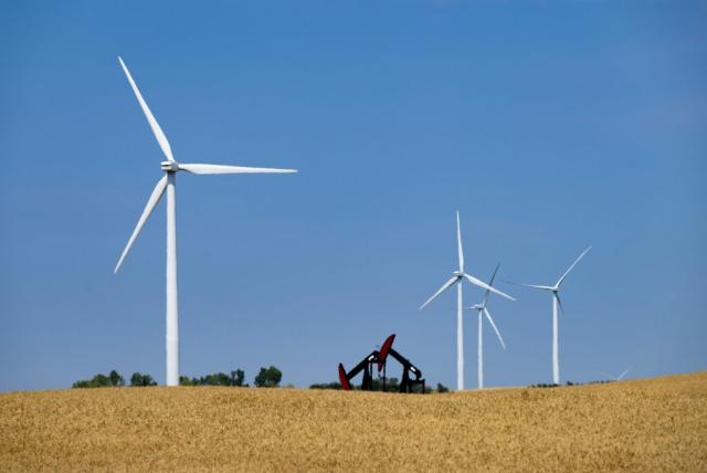 Four large wind turbines stand in a golden field, with two oil pump jacks in the distance