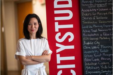 SuJan, arms folded beside a CityStudio banner and a chalkboard