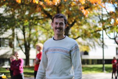 Alex Bigazzi, in a sweater among a tree-laden path
