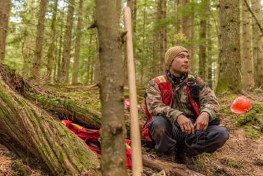 An IBPOC youth squatting in a forest