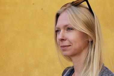 A woman with sunglasses atop her head, in a grassy walkway