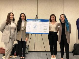 Four young women posing beside a project poster