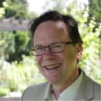 Michael, in tan suit, smiling among trees